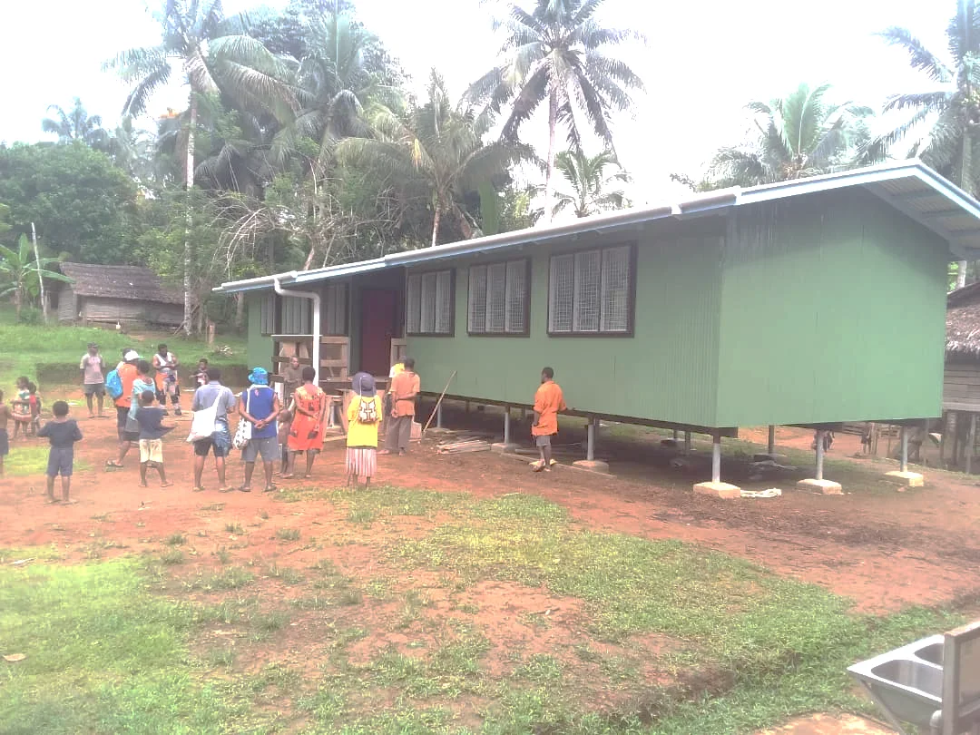 A raised classroom building with people gathered outside.
