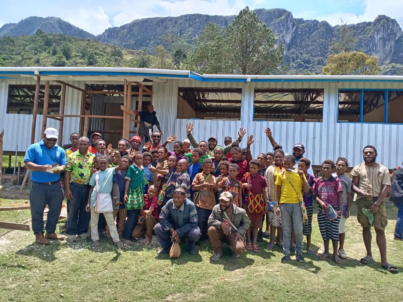 Community members gathered outside a classroom building, with mountains in the background.